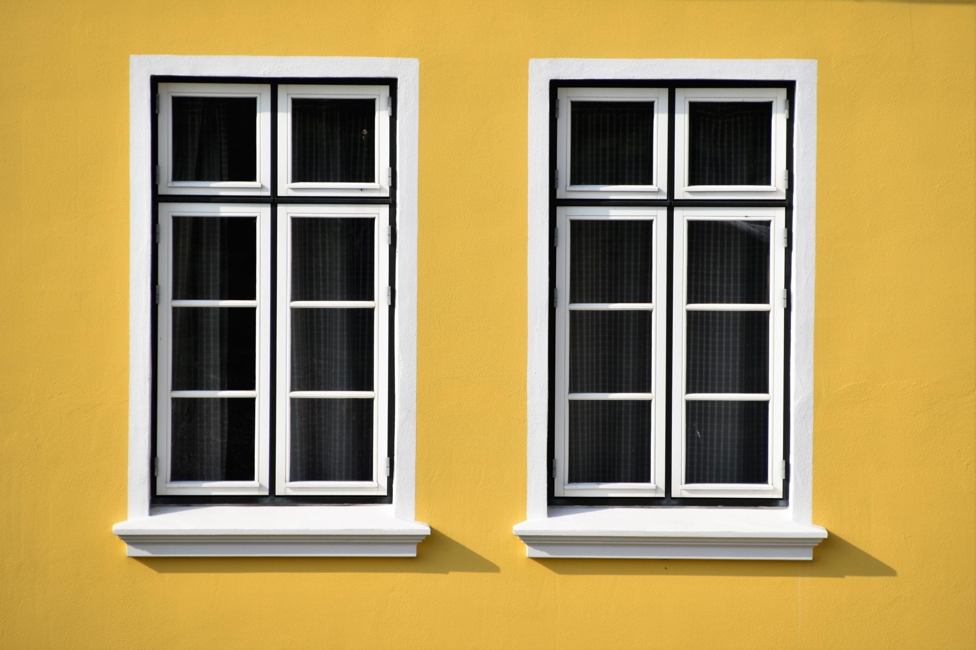 two black windows on the front of a yellow house